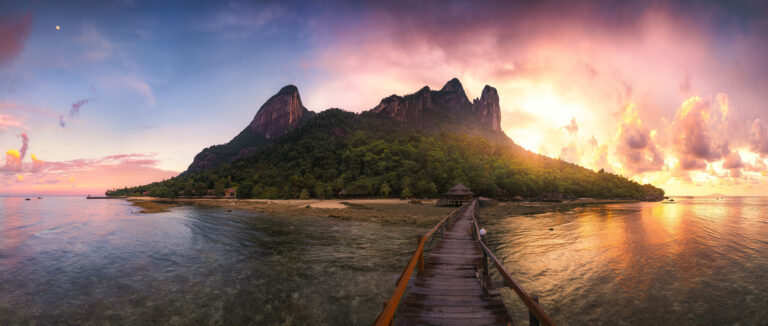 Paradiesisches Inselpanorama von Pulau Tioman mit den ikonischen Felsbergen und üppiger tropischer Vegetation in stimmungsvollem warmen Sonnenaufgangslicht