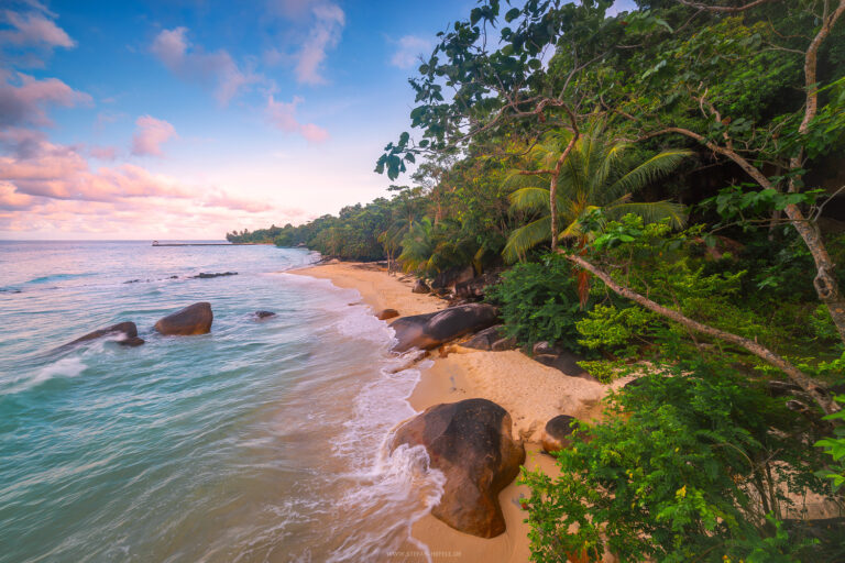 Paradiesische Bucht mit rötlichen Felsen, Palmen und tropischer Vegetation auf der Malaysischen Insel Pulau Tioman im stimmungsvollem Licht