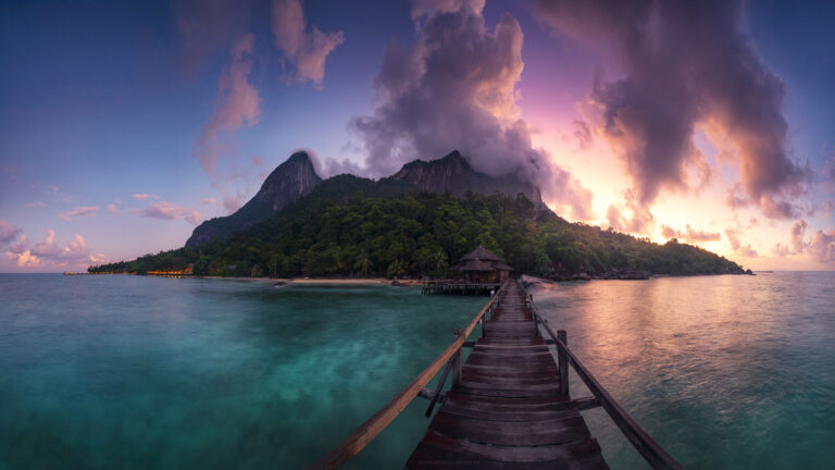 Paradiesisches Inselpanorama von Pulau Tioman mit den ikonischen Felsbergen und üppiger tropischer Vegetation in stimmungsvollem purpurnem Sonnenaufgangslicht