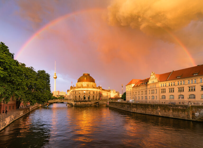 Sonnenuntergang mit Regenbogen in Berlin über der Museumsinsel mit Fernsehturm im HG in malerisch-bunter Stimmung. Aufziehendes Unwetter mit düsteren Wolken